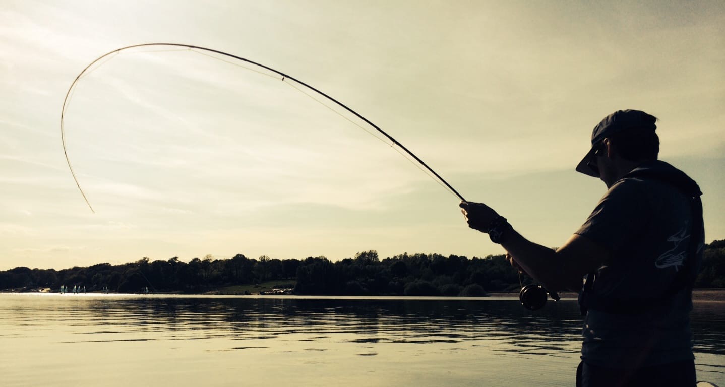 James Marcheselli fly fishing at dawn or dusk, rod bent, reflected on still water